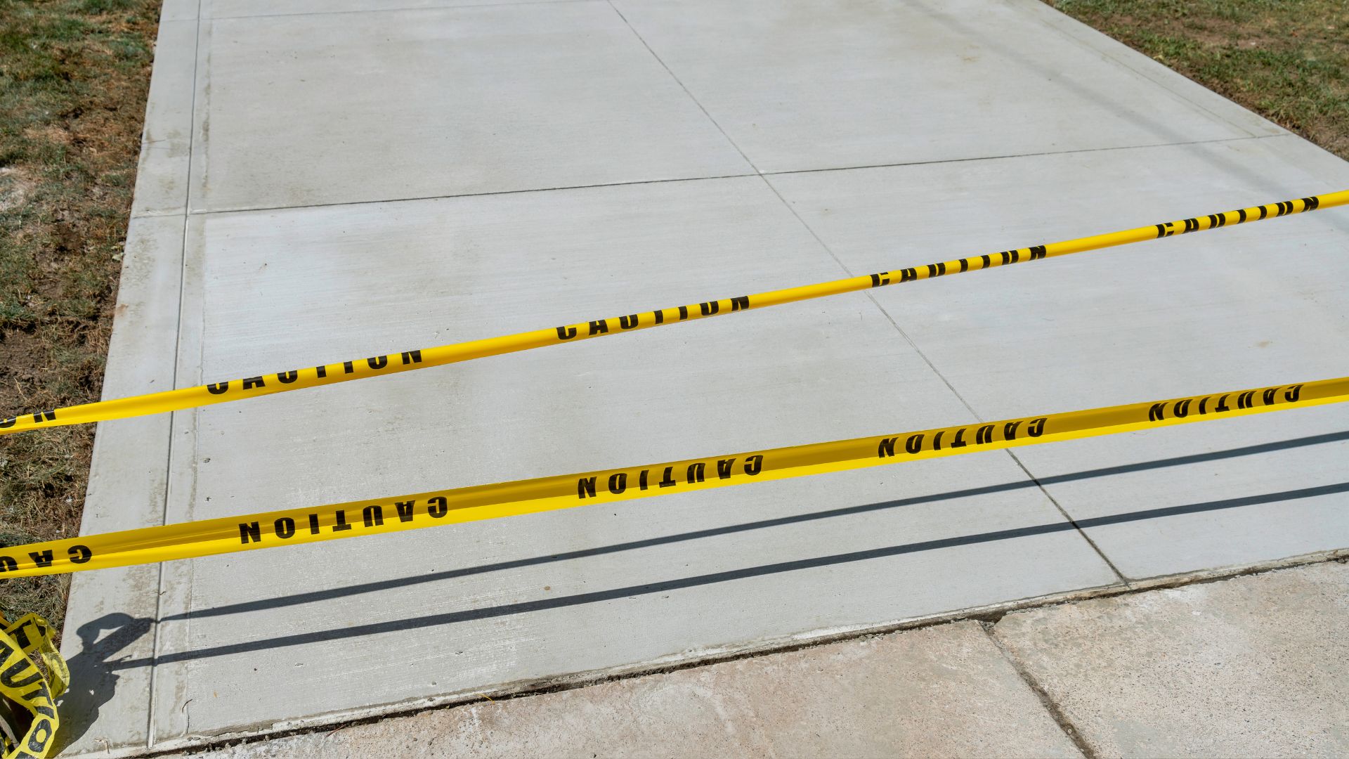 Yellow caution barricades on a sidewalk with grass in the background